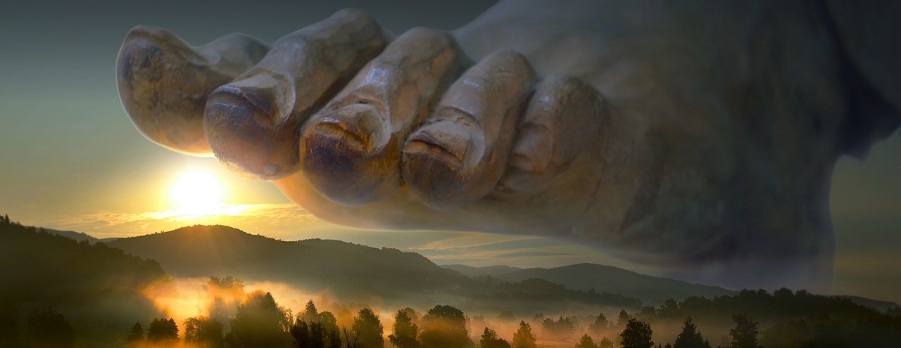 A giant foot bearing down on a vast mountain landscape as the sun rises